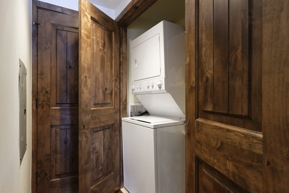 A laundry closet with wooden doors partially open revealing a stacked washer and dryer unit inside.