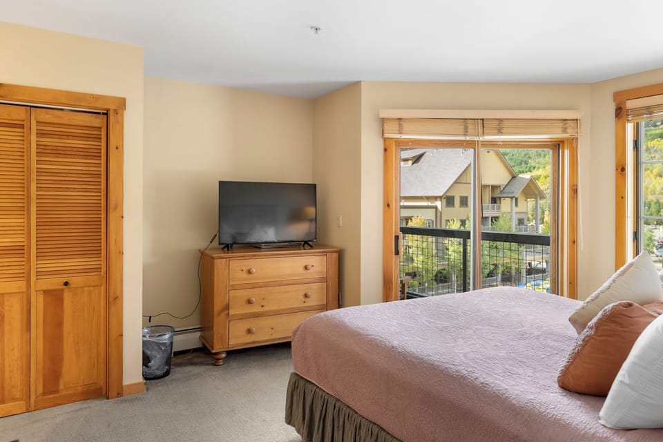 Cozy bedroom with warm wood accents where you'll unwind watching TV after mountain adventures, with peaceful neighborhood views.