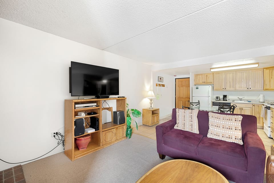 Relax in your cozy living space with a plush purple sofa, large TV, and fully equipped kitchen ready for home-cooked meals.