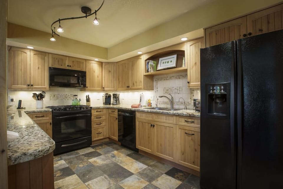 View into the kitchen with refrigerator, double sink, dishwasher, 4-eye gas stovetop, microwave, oven, coffee maker, Keurig machine, blender, and toaster.