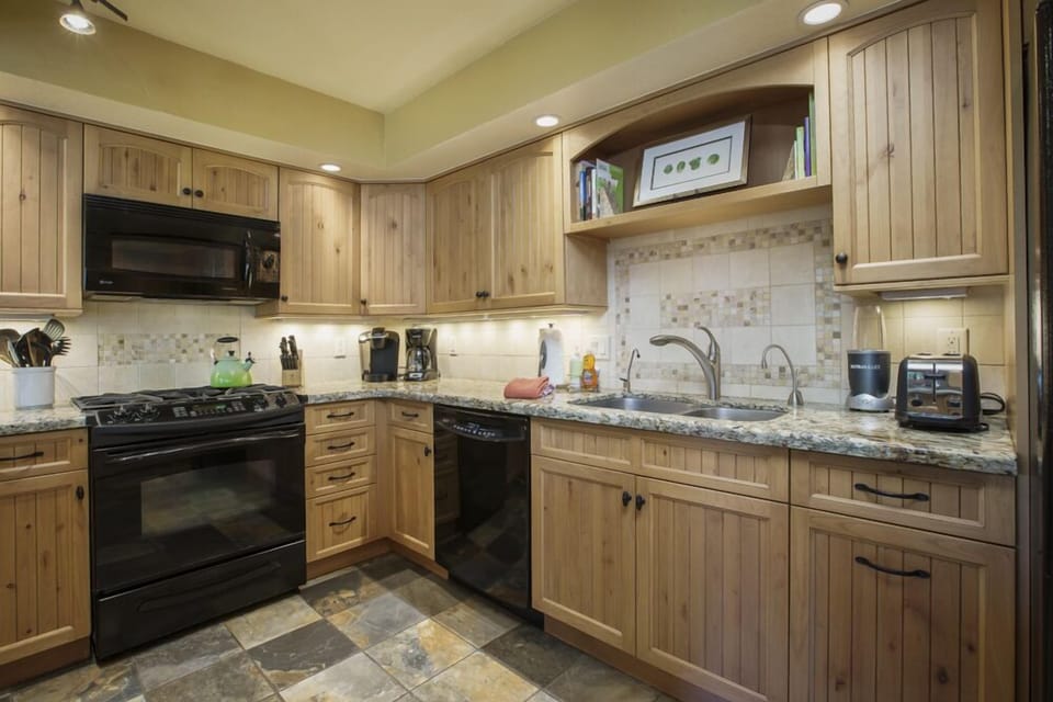 View into the kitchen with refrigerator, double sink, dishwasher, 4-eye gas stovetop, microwave, oven, coffee maker, Keurig machine, blender, and toaster.