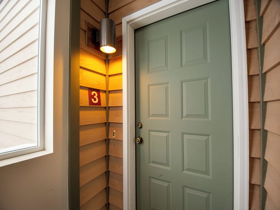 Welcoming sage green door marks your arrival, beautifully lit by warm porch lighting that guides you home after exploring.