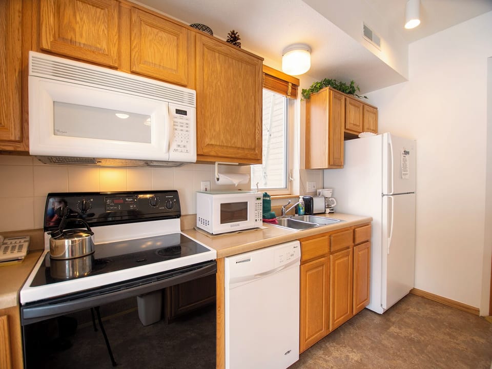 Your fully equipped kitchen features everything you need to prepare delicious meals, with warm wood cabinets and modern white appliances creating a welcoming space.
