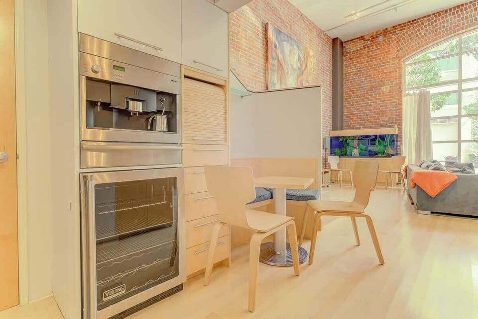 Open loft dining area with modern kitchen, exposed brick, and bright windows—stylish, welcoming, and perfect for shared meals.