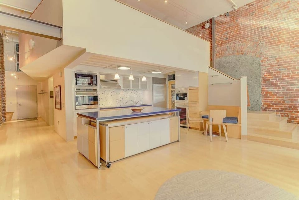 Modern open kitchen with sleek island, warm lighting, and exposed brick—bright, stylish, and ideal for cooking and gathering.