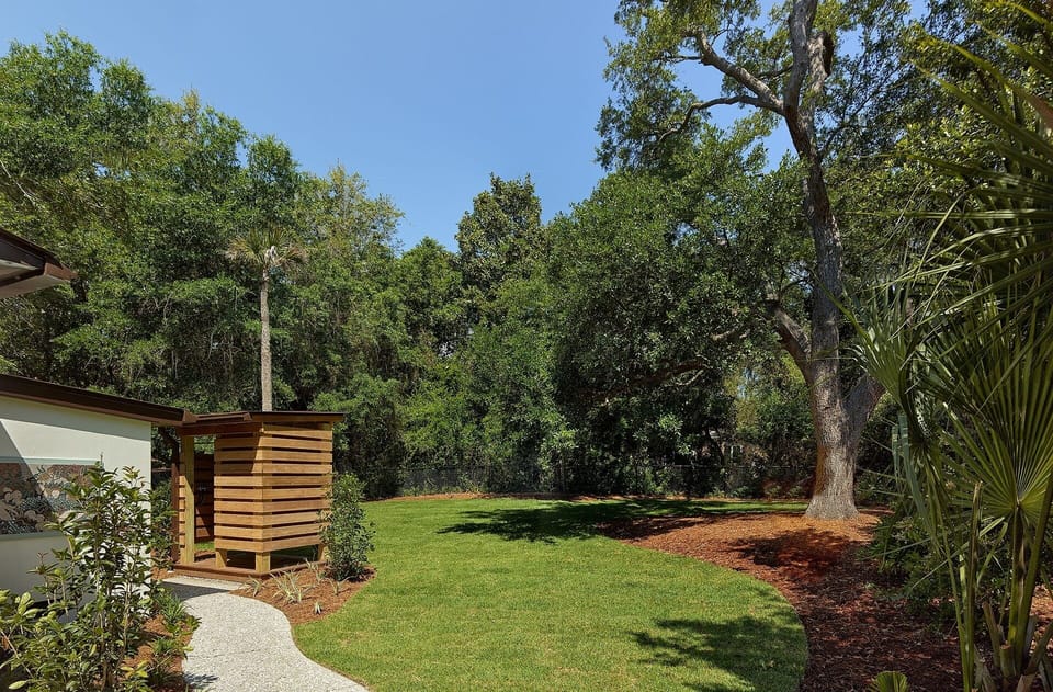 The fenced in backyard is beautifully landscaped and features a Hot/Cold private rain outdoor shower in addition to the patio area with tables and seating.