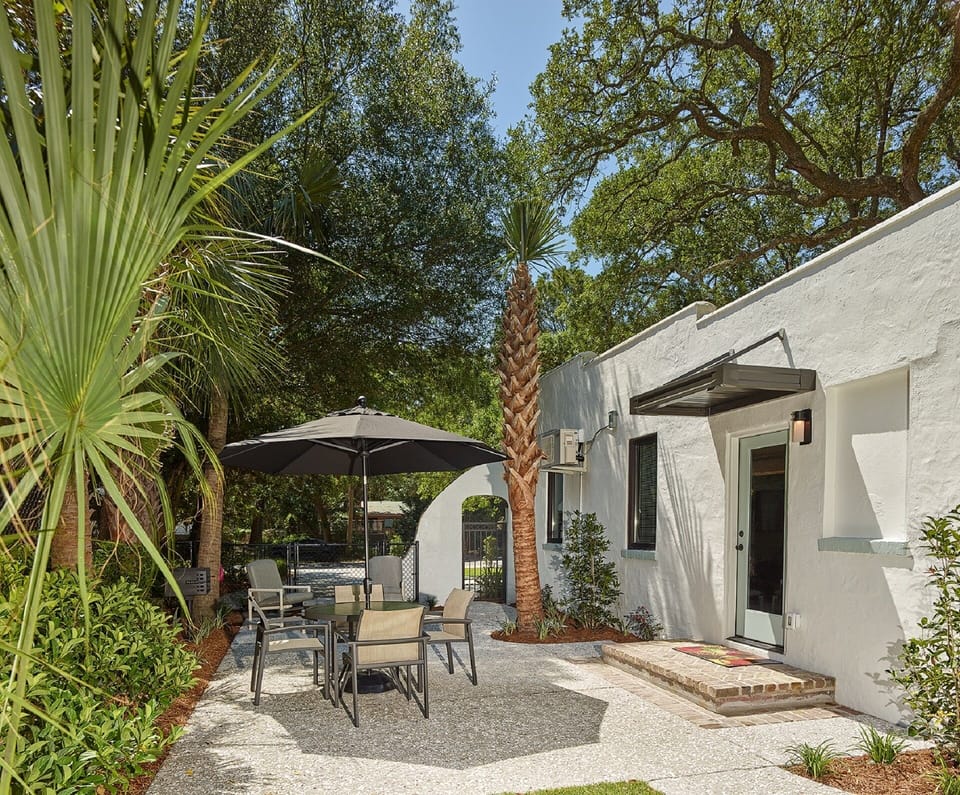 The fenced in yard has a four person table with umbrella and charcoal grill.
