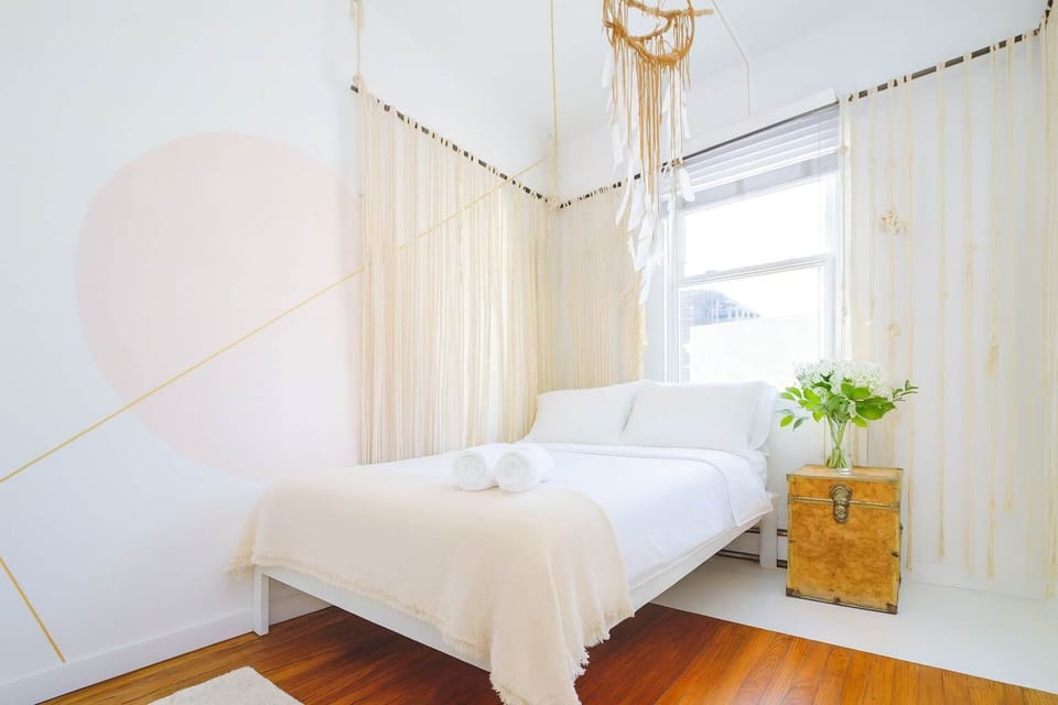 Serene, light-filled bedroom with cozy white linens, warm wood floors, and soft natural accents—clean, calming, and beautifully styled.
