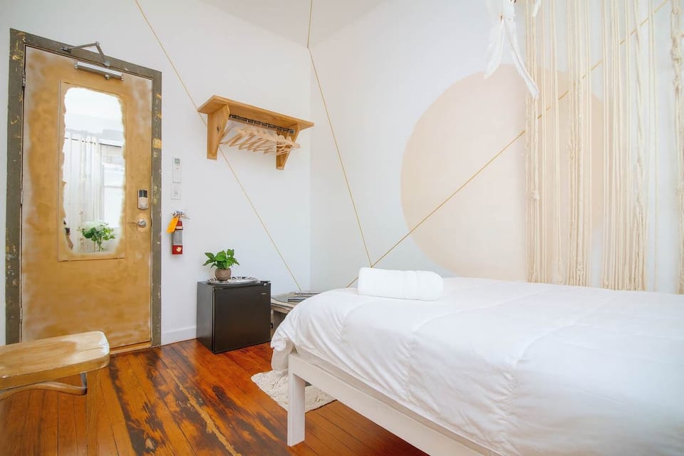 Bright, minimalist bedroom with cozy white bedding, warm hardwood floors, and artistic accents—clean, calm, and inviting.
