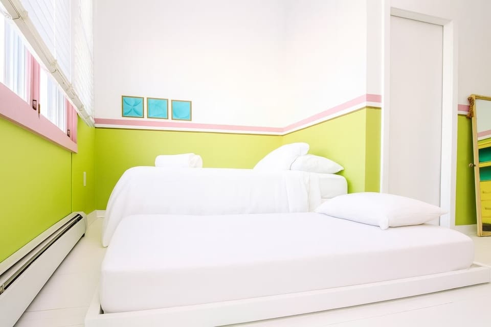 Fresh, playful bedroom with bright green accents, cozy beds, and soft white linens—cheerful, clean, and ideal for families or friends.
