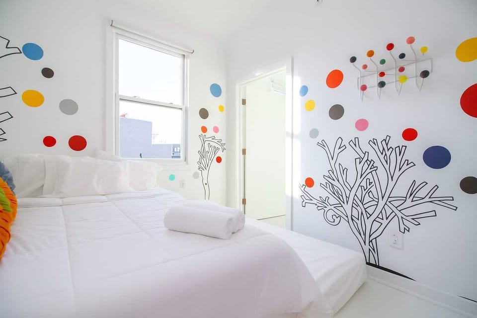 Bright, whimsical bedroom with colorful wall art, cozy bed, and natural light—clean, cheerful, and creatively designed.
