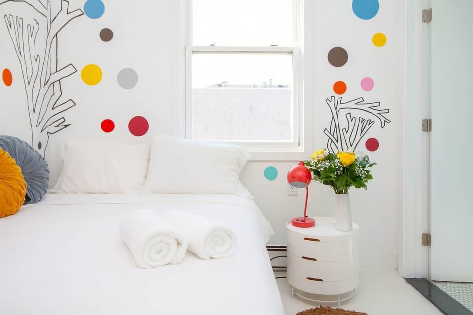Bright, cheerful bedroom with playful wall art, cozy bed, and sunny window—clean, inviting, and thoughtfully styled.
