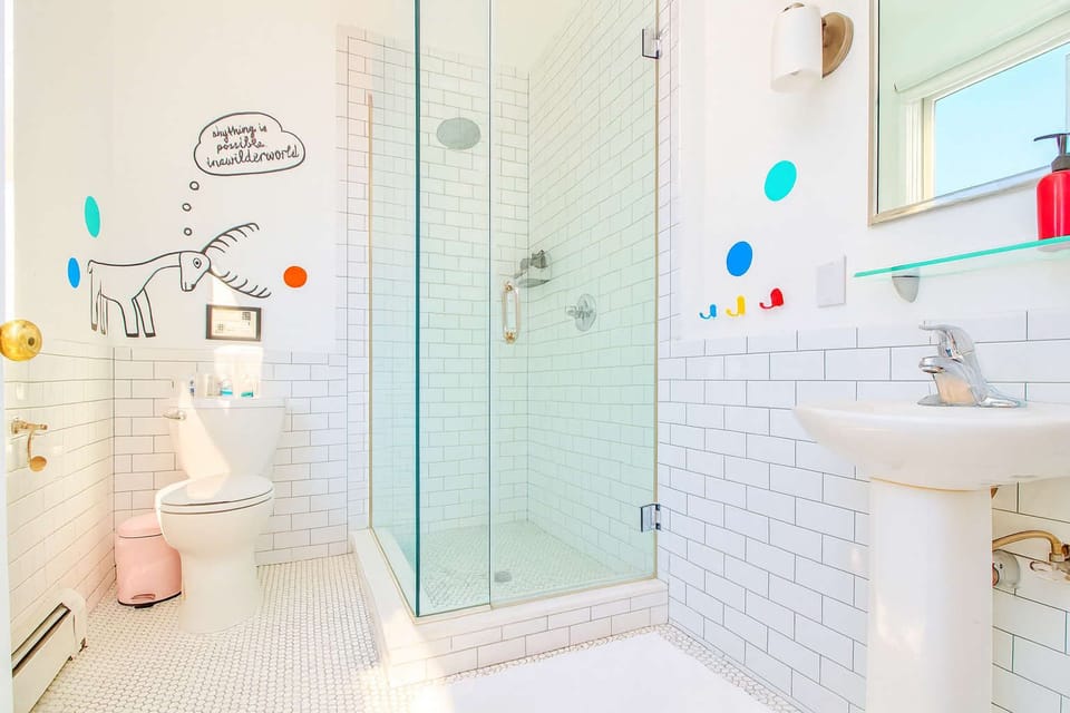 Bright, playful bathroom with subway tile, glass shower, and fun wall art—clean, modern, and full of character.
