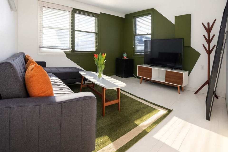 Sunlit living room with modern furnishings, bold green accents, and cozy seating—bright, stylish, and perfect for relaxing.
