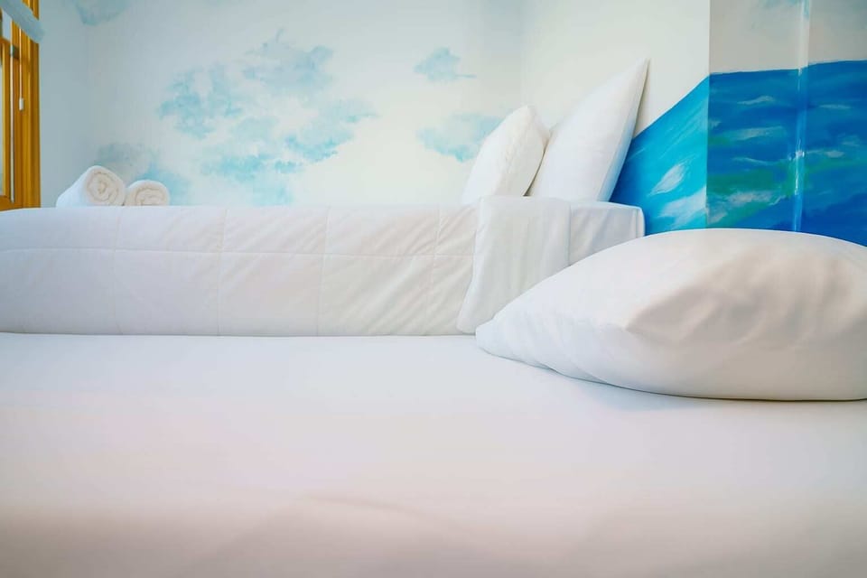 Bright, ocean-themed bedroom with crisp white linens and soothing mural—clean, cozy, and designed for restful coastal stays.
