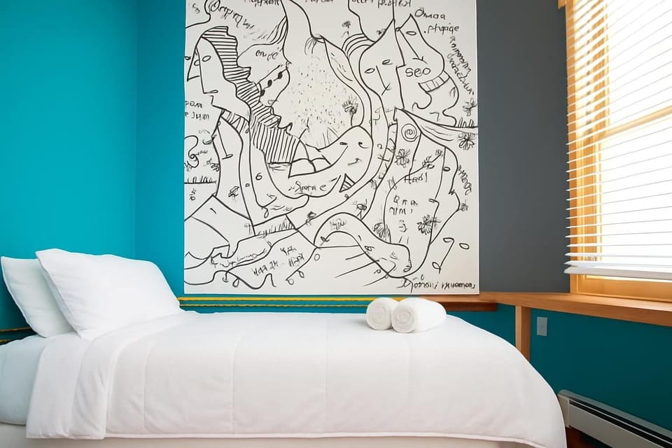 Modern, artistic bedroom with custom wall art, cozy bed, and fresh white linens—stylish, bright, and uniquely designed.
