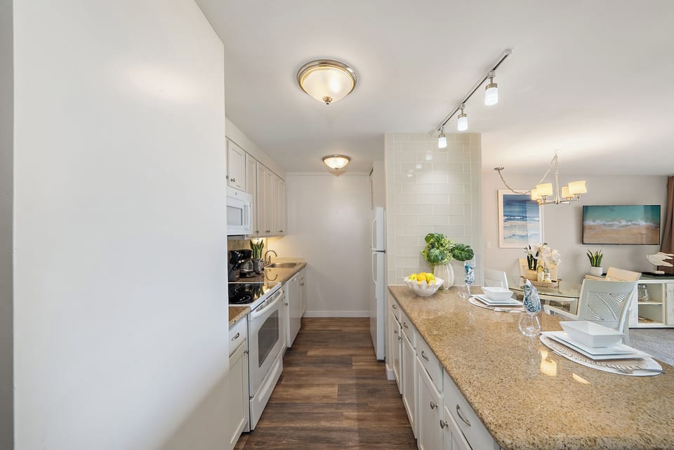 Fully furnished kitchen with white appliances, white cabinets and granite countertops