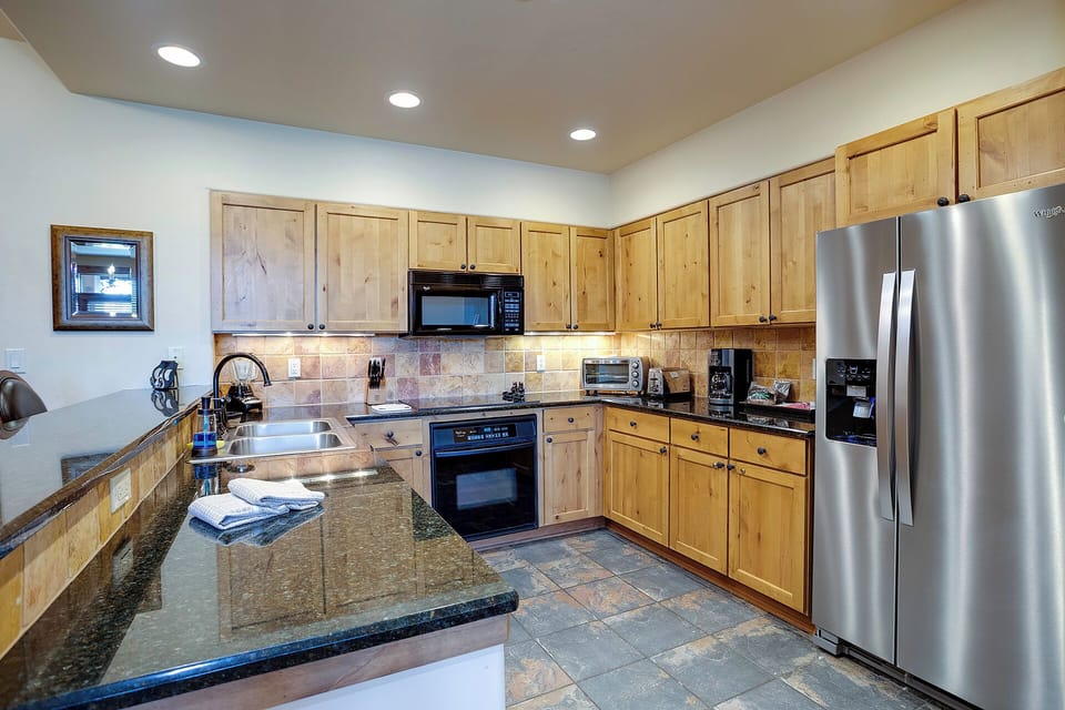 Your fully equipped kitchen awaits with granite counters, stainless appliances, and warm wood cabinets - perfect for preparing memorable meals during your stay.