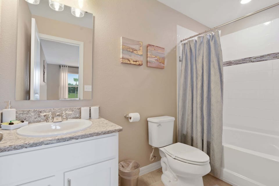 Bright, spotless full bathroom with tub/shower, granite-style vanity and neutral tiles-modern, clean design for quick refreshes during your stay.