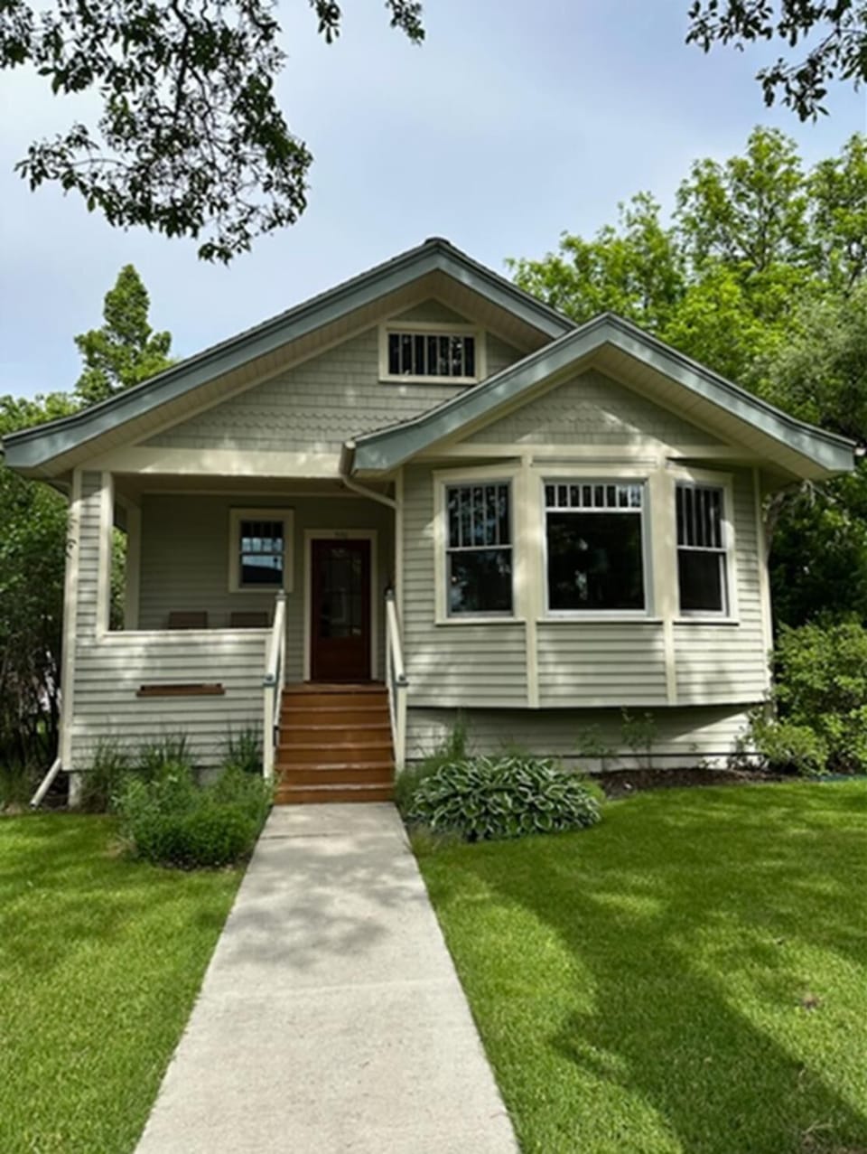 Concrete walkway leads to wooden steps and a covered front porch with beige siding and white trim.