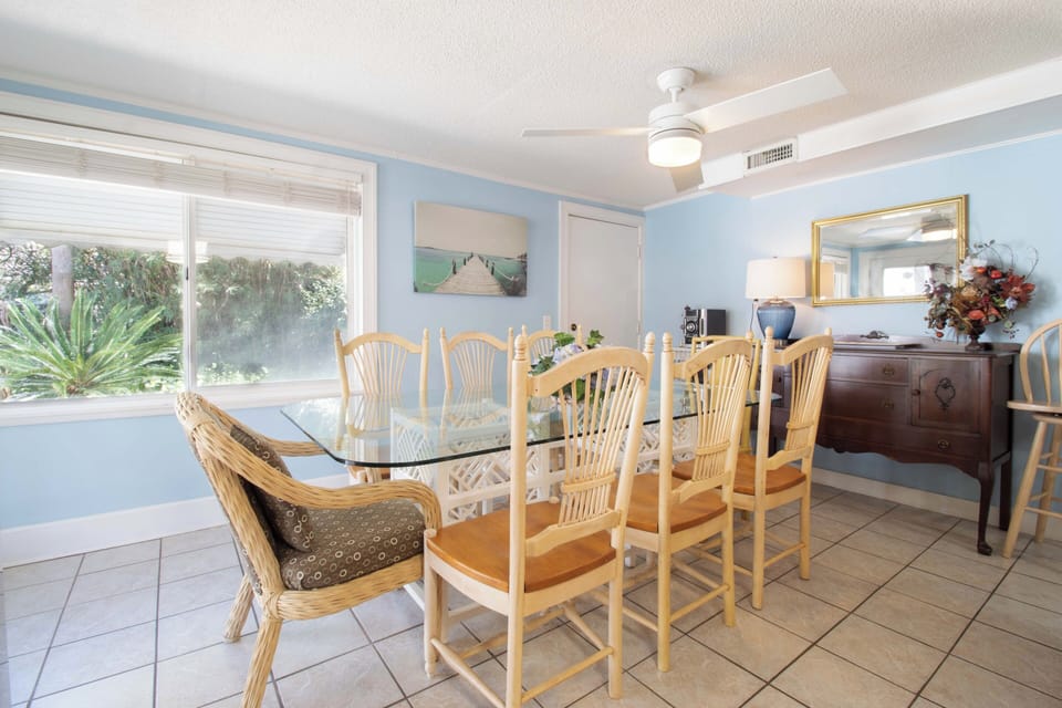 Gather around your elegant glass dining table where tropical views through large windows create the perfect backdrop for memorable meals together.