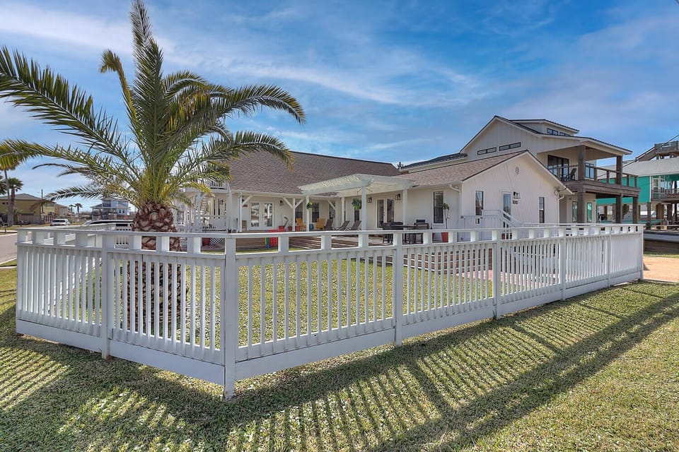 Exterior - Inviting fenced yard with covered patio, outdoor seating, and tropical landscaping — perfect for family gatherings, cookouts, or letting the kids play safely in the sea breeze of Port Aransas.