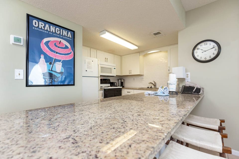 The kitchen features granite countertops, modern appliances, and a vibrant vintage poster, perfect for meal prep or gathering