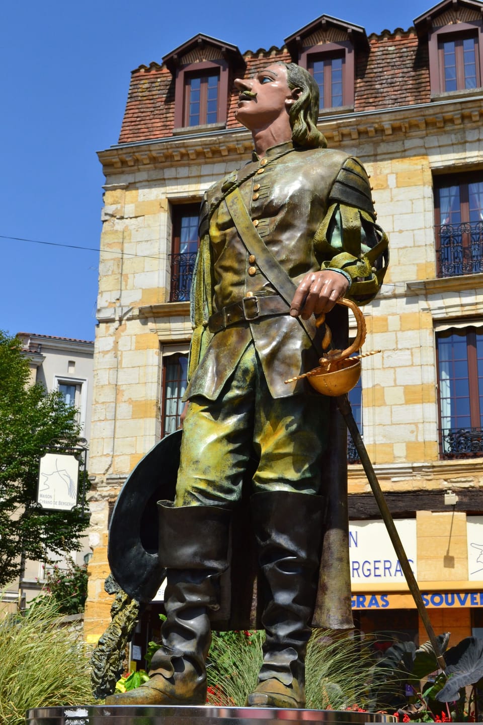 Bronze statue of Cyrano de Bergerac in period costume standing in the town square