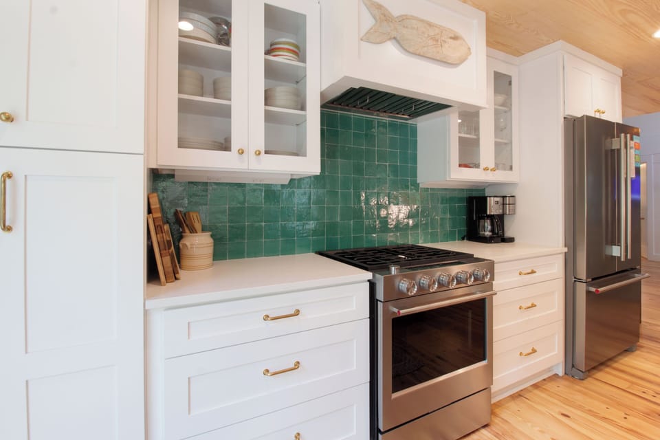 Your fully equipped kitchen awaits with striking teal tile backsplash, stainless steel appliances, and coastal charm—perfect for preparing meals and gathering with loved ones.