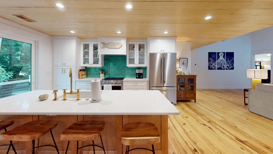 Step into a bright, modern kitchen with gleaming white counters and warm wood floors. The turquoise backsplash adds a splash of coastal charm, while the open layout flows seamlessly into your cozy living area.