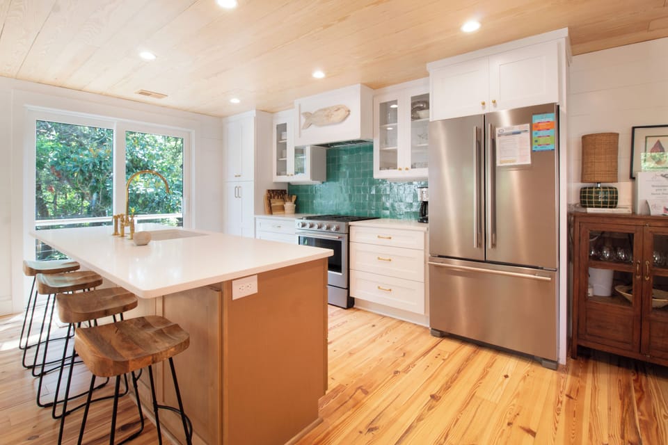 Step into your fully equipped kitchen with gleaming stainless appliances, sunny island seating, and beautiful teal tile backsplash—where morning coffee and meal prep feel effortless.