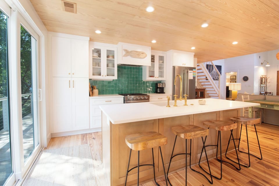 Your fully-equipped kitchen invites effortless meal prep, with a spacious island for casual dining under warm wood ceilings and soft recessed lighting.