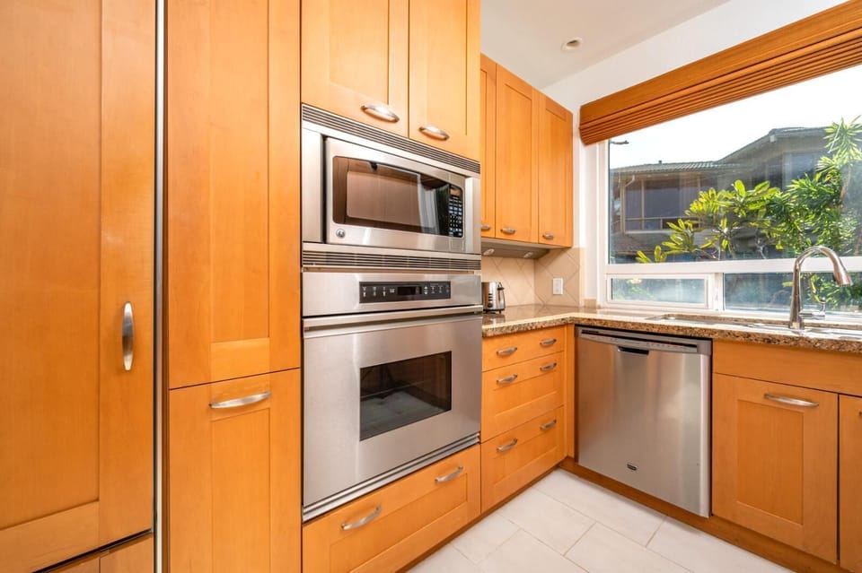 Cook in style with granite countertops, custom wood cabinetry, and large windows that bring paradise indoors    