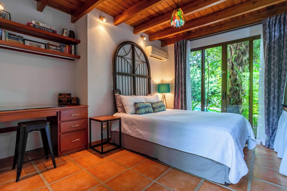 Bedroom #2 with desk/workspace, ac, queen bed and doors open to pool and garden.