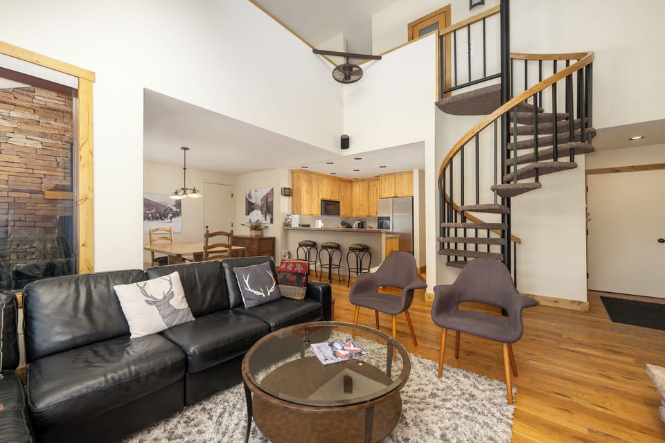 Relax in your stylish open-concept living space with soaring ceilings, modern spiral staircase, and seamless flow to the fully-equipped kitchen.