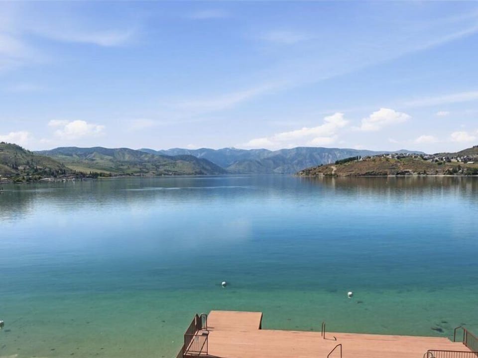 Serene lake view framed by distant mountains, with a private dock extending into crystal-clear turquoise waters—perfect for morning swims and peaceful afternoons by the shore.