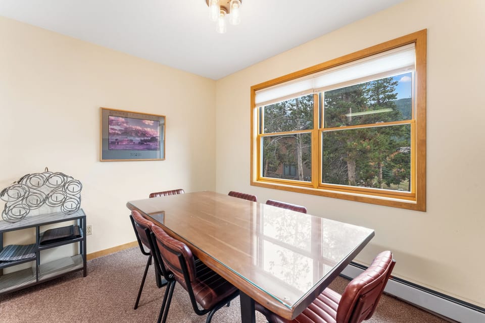 Gather around your spacious dining table for memorable meals, with warm natural light streaming through the window overlooking peaceful treetops.