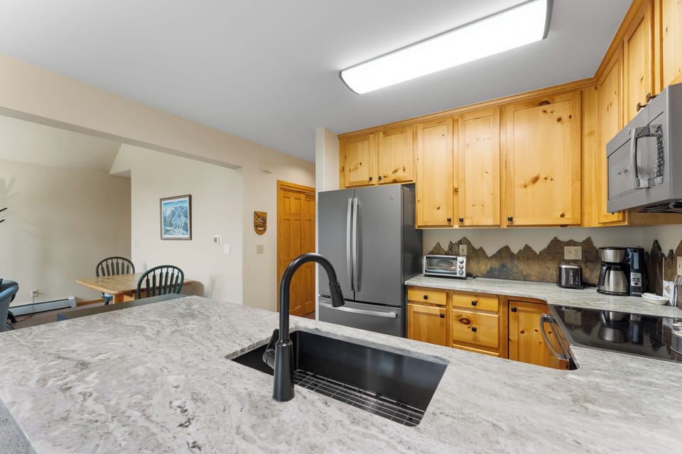 Your fully equipped kitchen features warm wood cabinets, granite counters, and mountain-themed backsplash for memorable meal preparation.