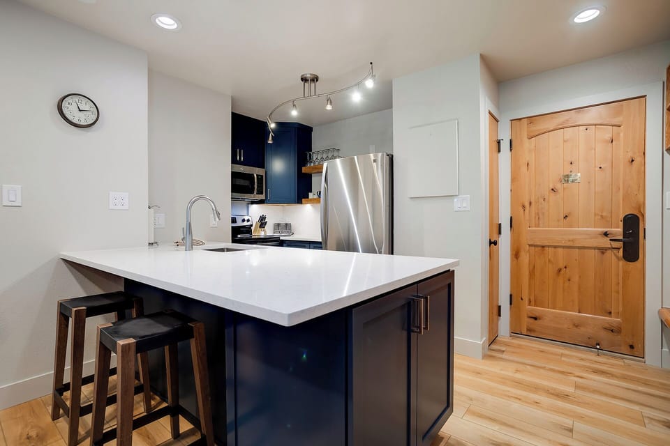 Your modern kitchen features a sleek island with seating, stainless steel appliances, and stylish navy cabinets perfect for culinary adventures.