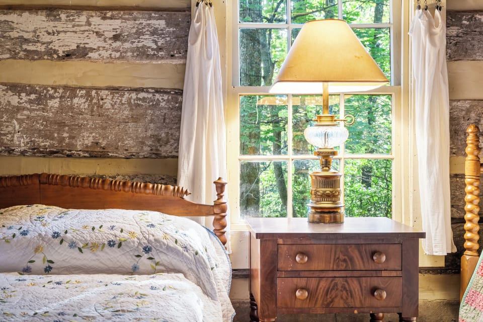 Romantic and serene log cabin bedroom with a four-poster bed, soft embroidered quilt, warm lamplight, and tranquil forest views—perfect for a peaceful mountain escape.