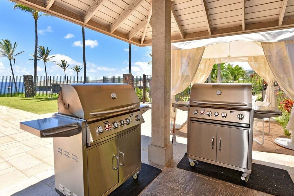 Convenient outdoor cooking area with multiple gas grills set beneath a covered pavilion near the pool.