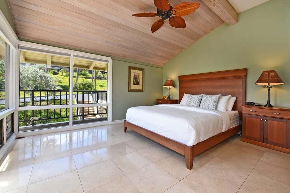 Spacious primary bedroom with a king-size bed, warm wood accents, ceiling fan, and peaceful garden views.