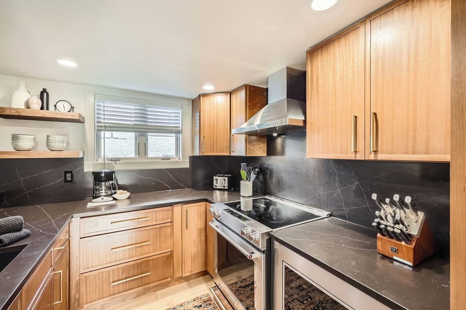 Fully equipped kitchen with sleek black quartz countertops, stainless steel appliances, and warm wood cabinetry — perfect for preparing meals or a morning coffee before hitting the slopes.