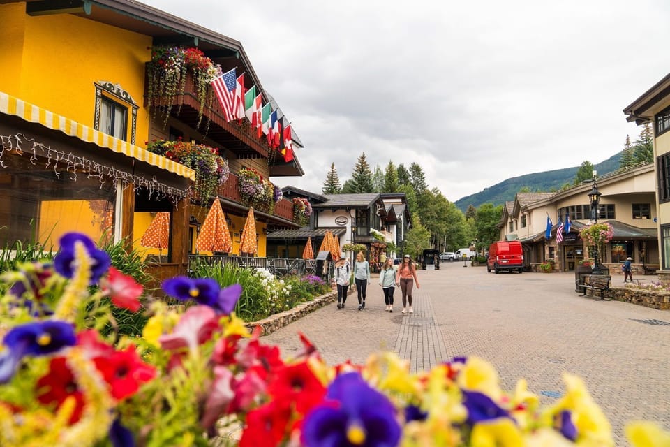 Flower-lined pedestrian street fronts alpine-style storefronts decorated with colorful hanging flags
