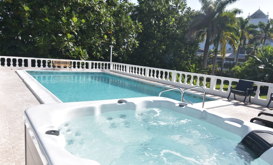 Poolside spa with swimming pool also pool furniture with BBQ pit to the left  