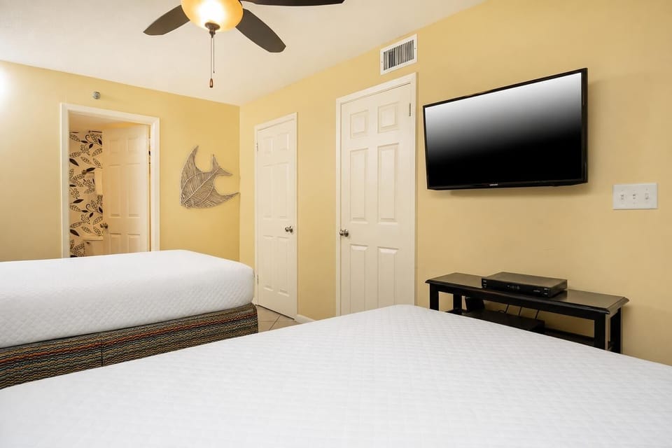 Cheerful guest bedroom featuring two comfortable queen beds, a TV, and vibrant decor for a relaxing stay