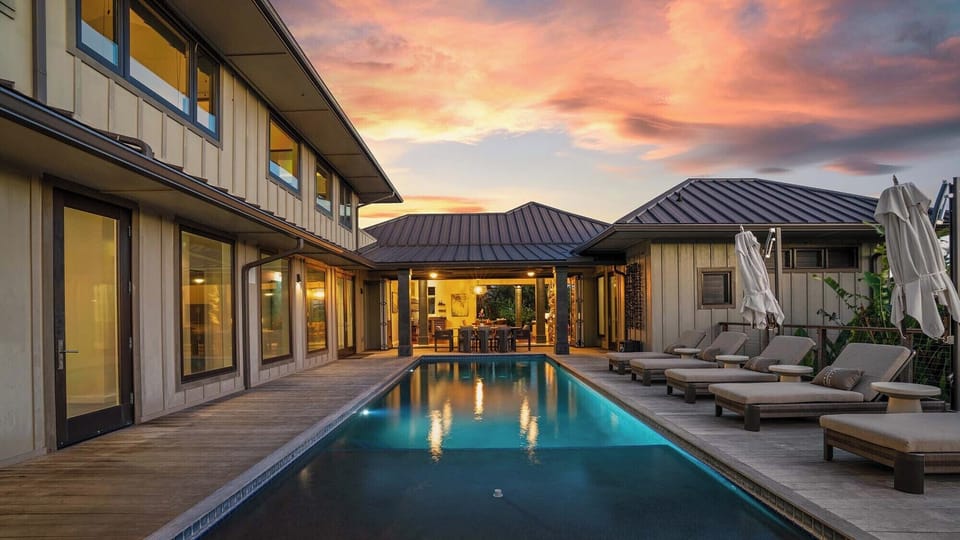 A stunning courtyard pool set against a dramatic sunset sky, bordered by elegant architecture and framed by tropical greenery defining the property's inviting outdoor centerpiece.
