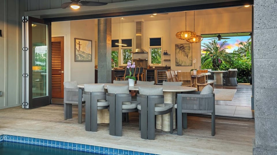 Poolside living flows seamlessly between indoors and out, with a stylish dining area and open kitchen bathed in warm evening light—your perfect spot for tropical gatherings.