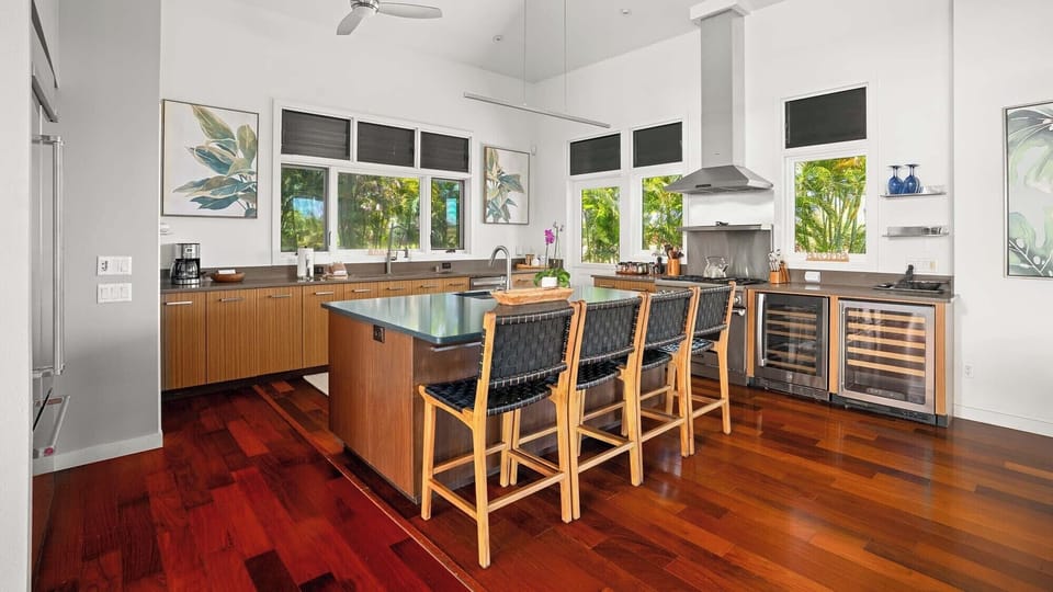 Your gourmet kitchen features rich hardwood floors, sleek cabinetry, and a spacious island perfect for gathering with family. Natural light pours through large windows, framing lush tropical views.