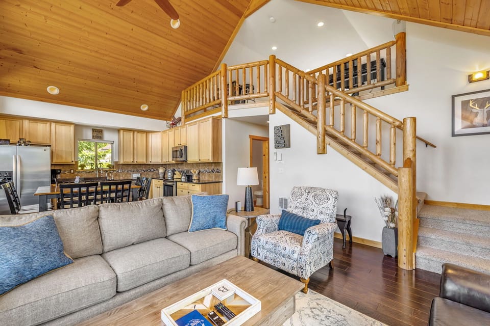 Open-concept living with exposed wood beams, cozy furnishings, and a rustic-style staircase centerpiece